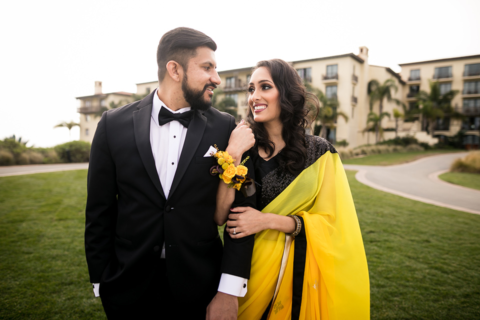 Terranea-styled-shoot-bride-and-groom-close-up-smiling-looking-at-each-other-bride-in-yellow-sarees-with-hair-in-a-loose-wave-groom-in-a-tradtitional-black-tuxedo-with-a-black-bowtie-and-black-vest