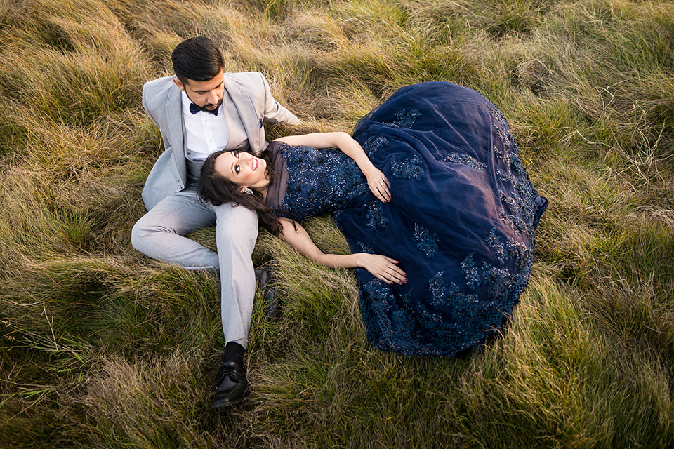 Terranea-styled-shoot-bride-and-groom-laying-in-the-grass-bride-in-a-midnight-blue-dress-with-an-illusion-neckline-with-jewels-on-bodice-her-hair-down-in-a-loose-wave-groom-in-a-light-grey-suit-with-a-blue-bow-tie-to-match-the-bride