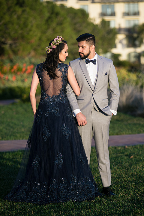 Terranea-styled-shoot-bride-in-blue-dress-and-crown-back-towards-to-the-camera-groom-in-grey-facing-camera-bride-in-a-midnight-blue-dress-with-an-illusion-neckline-with-jewels-on-bodice-her-hair-down-in-a-loose-wave-groom-in-a-light-grey-suit-with-a-blue-bow-tie-to-match-the-bride