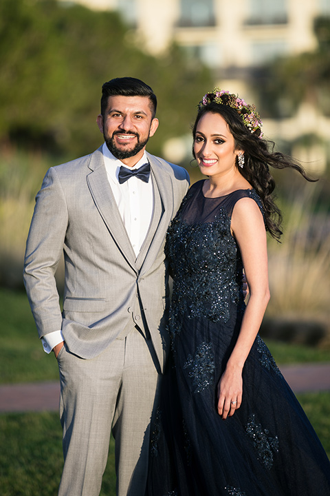 Terranea-styled-shoot-grey-and-blue-looks-both-smiling-at-camera-bride-in-a-midnight-blue-dress-with-an-illusion-neckline-with-jewels-on-bodice-her-hair-down-in-a-loose-wave-groom-in-a-light-grey-suit-with-a-blue-bow-tie-to-match-the-bride