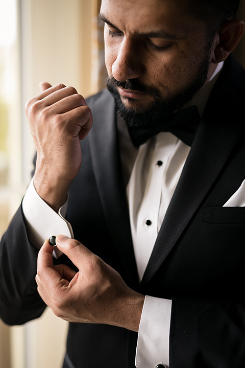 Terranea-styled-shoot-groom-fixing-cufflinks-groom-in-a-traditonal-black-tuxedo-with-black-bow-tie-and-black-studs-and-cufflinks