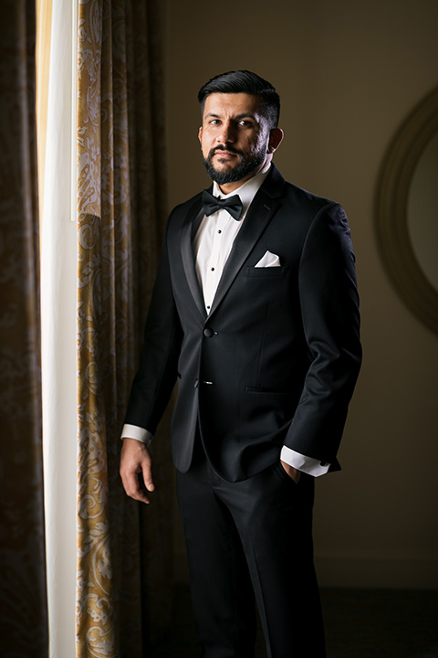 Terranea-styled-shoot-groom-looking-at-camera-groom-fixing-cufflinks-groom-in-a-traditonal-black-tuxedo-with-black-bow-tie-and-black-studs-and-cufflinks