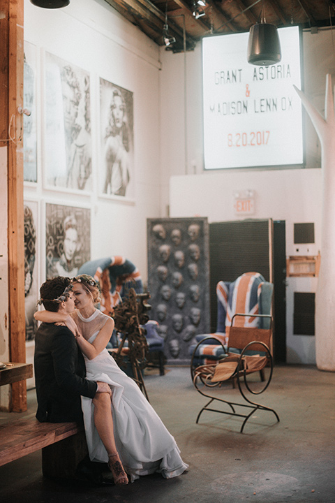 Voila-studios-bride-sitting-on-grooms-lap-bride-in-a-flowing-gown-with-a-natural-waistline-and-an-illusion-neckline-with-a-floral-crown-groom-in-a-navy-tuxedo-with-a-leather-bow-tie