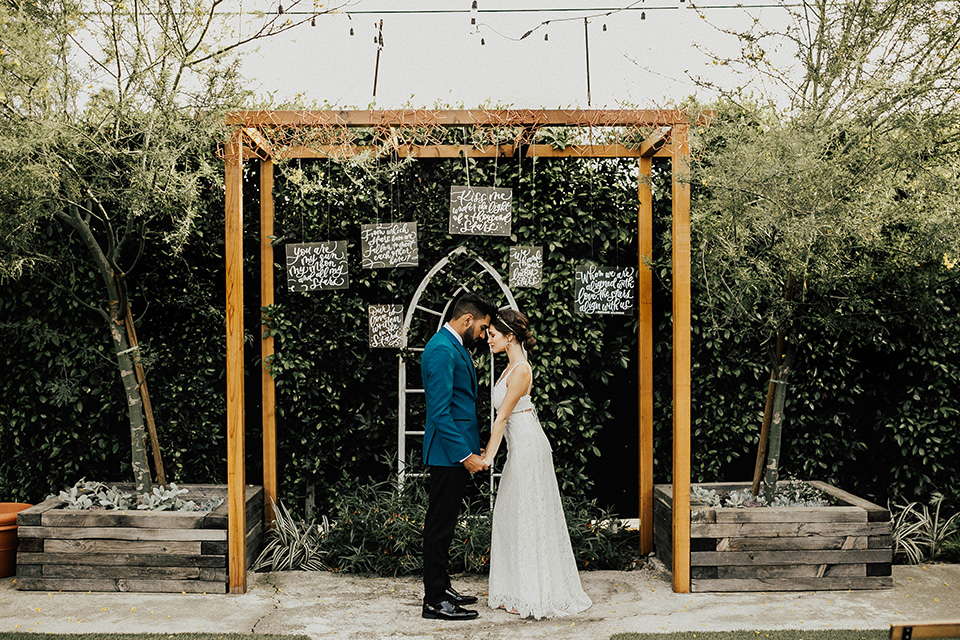 The-Ruby-Street-photoshoot-bride-and-groom-under-ceremony-arch-groom-in-a-teal-tuxedo-with-black-pants-and-bride-in-a-lace-bohemian-dress