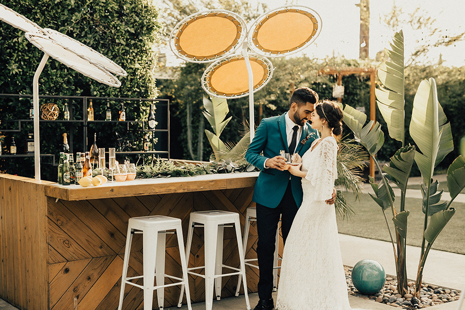 The-Ruby-Street-photoshoot-couple-outside-by-bar-groom-in-a-teal-tuxedo-with-black-pants-and-bride-in-a-lace-bohemian-dress