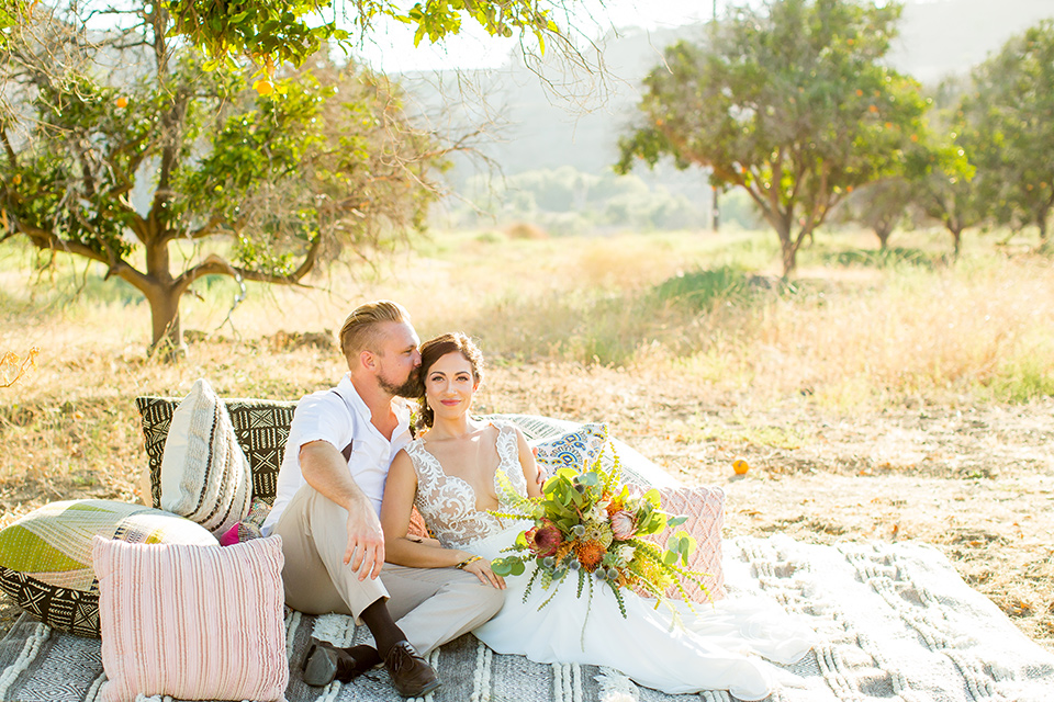 A-Stones-Throw-Winery-African-Shoot-bride-and-groom-sitting-on-blanket-with-pillows-bride-in-an-a-line-gown-with-lace-straps-groom-in-a-tan-suit-with-brown-accessories-and-susenders