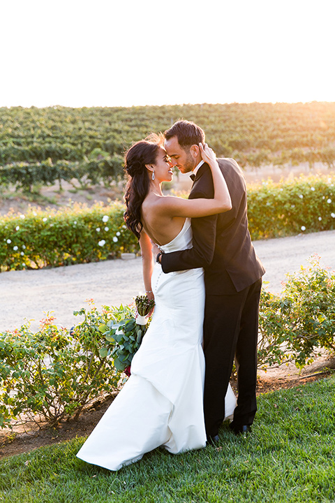 Villa-de-Amore-bride-and-groom-kissing-with-sun-setting-bride-and-groom-by-ivy-bride-in-a-fitted-gown-groom-in-a-black-tuxedo