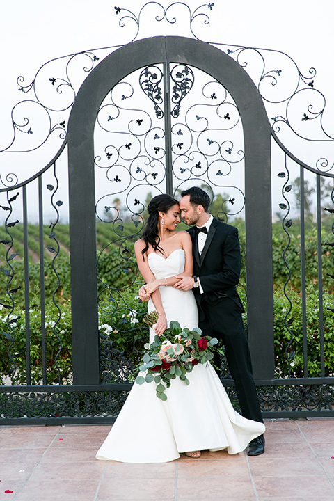 Villa-de-Amore-couple-touching-heads-by-iron-gate-bride-in-a-fitted-gown-groom-in-a-black-tuxedo