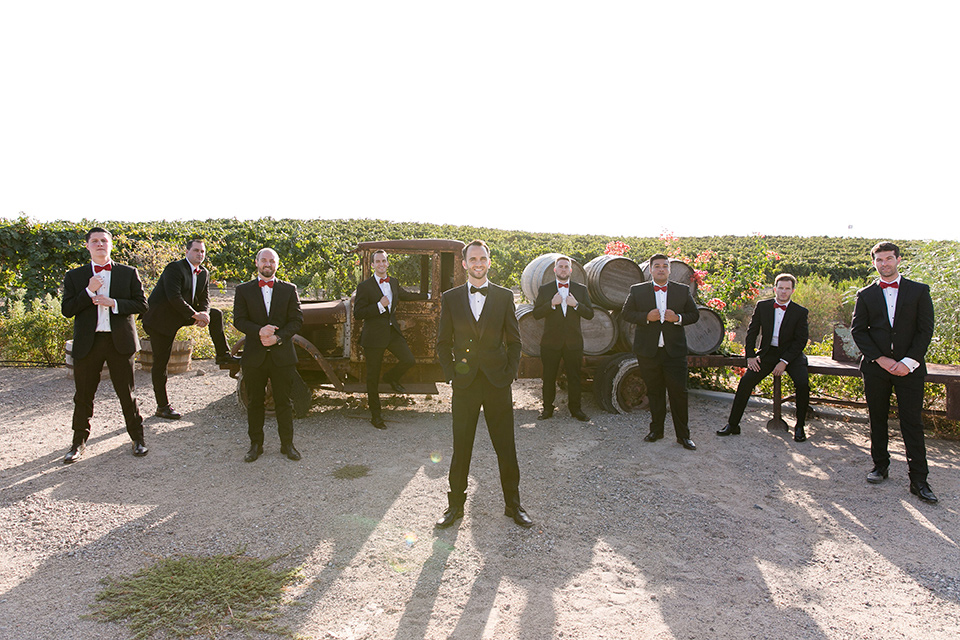 Villa-de-Amore-groomsmen-by-outdoor-décor-groom-in-black-tuxedo-with-black-bow-tie-and-groomsmen-in-black-tuxedo-with-red-bow-tie