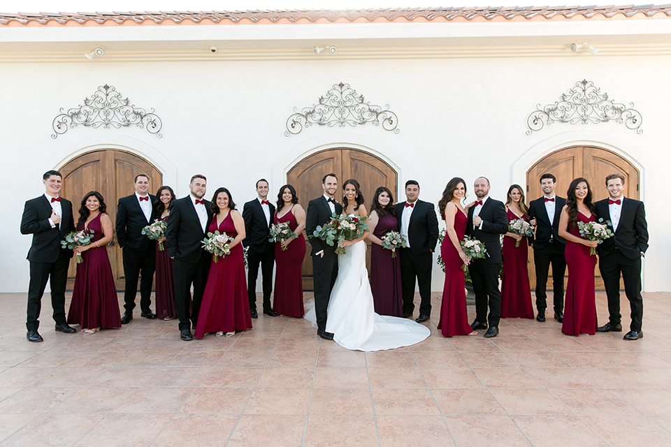villa-de-Amore-bridalparty-bride-in-a-strapless-gown-with-bridesmaids-in-alternating-red-dresses-groom-and-groomsmen-in-black-tuxedos
