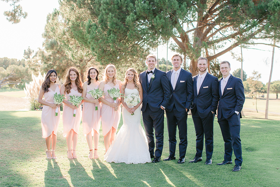 Los-Verdes-Golf-Course-Wedding-bridal-party-bridesmaids-in-light-pink-short-dresses-groomsmen-in-blue-suits-with-light-pink-bowties-bride-is-in-a-lace-mermaid-style-gown-with-a-modified-sweetheart-neckline-the-groom-is-in-a-navy-blue-tuxedo-with-a-black-shawl-lapel-and-a-black-bow-tie
