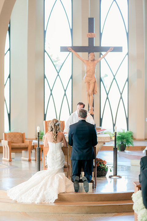 Los-Verdes-Golf-Course-Wedding-bride-and-groom-kneeling-at-ceremony-the-bride-is-in-a-lace-mermaid-gown-with-a-modified-sweetheart-neckline-and-the-groom-is-in-a-navy-blue-shawl-lapel-tuxedo