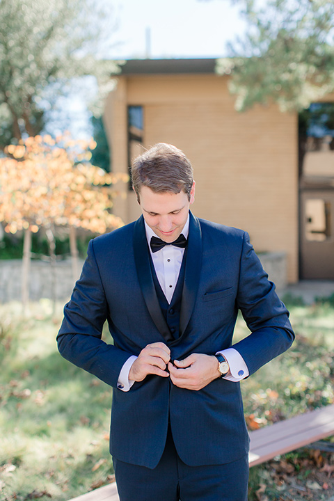 Los-Verdes-Golf-Course-Wedding-groom-buttoning-jacket-in-a-navy-blue-shawl-lapel-tuxedo-and-black-bow-tie