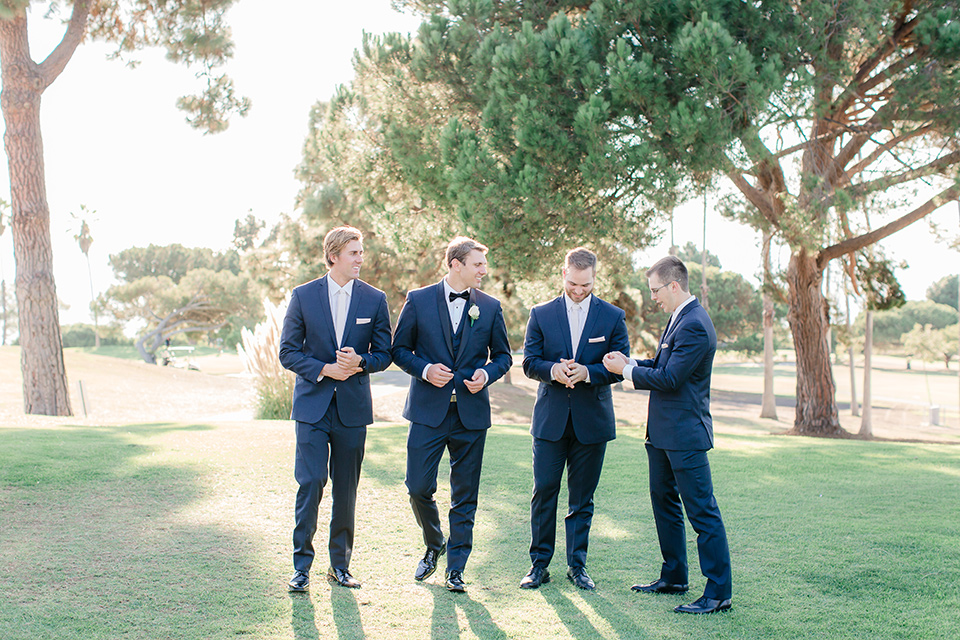 Los-Verdes-Golf-Course-Wedding-groomsman-walking-groomsmen-in-navy-blue-suits-the-groom-is-in-a-navy-blue-tuxedo-with-a-black-shawl-lapel-and-a-black-bow-tie