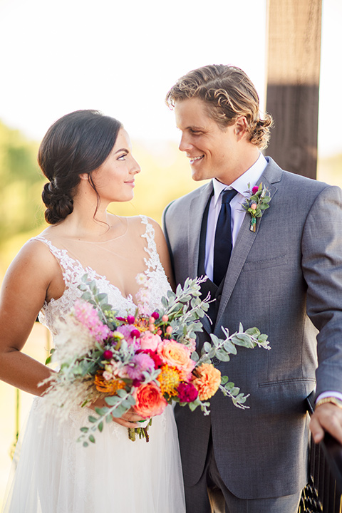 aliso viejo wedding design with the bride in a lace white gown with thin straps and a full skirt and the groom in a grey suit and navy neckline