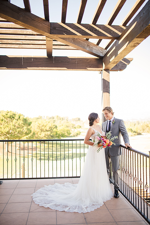 aliso Viejo wedding design with the bride and groom on the patio the bride is in a lace gown with thin straps and the groom in a grey suit with a navy neck tie