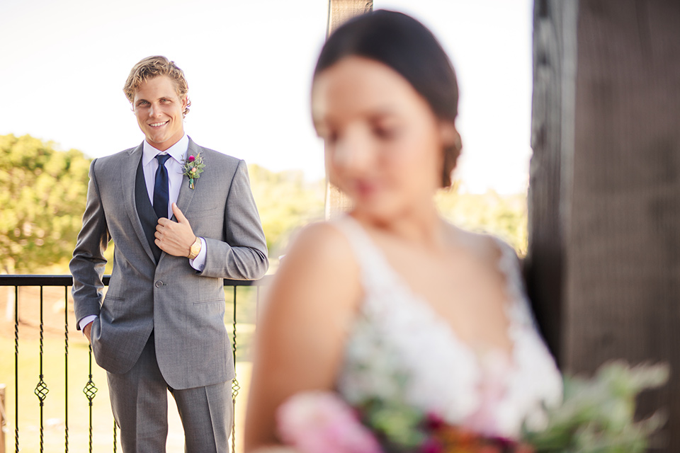 Aliso Viejo wedding design with the bride  and groom outside the bride in a lace gown with thin straps and the groom in a grey suit with a blue neck tie