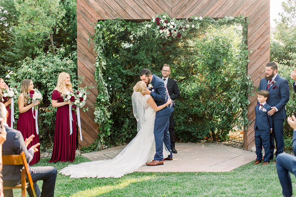 Burgundy-and-Blue-wedding-bride-and-groom-at-ceremony-brdesmaids-in-burgundy-gowns-groomsmen-in-dark-blue-suits-bride-in-a-formfitting-white-lace-gown-with-a-strapless-neckline-the-groom-is-in-a-dark-blue-suit-with-an-ivory-long-tie