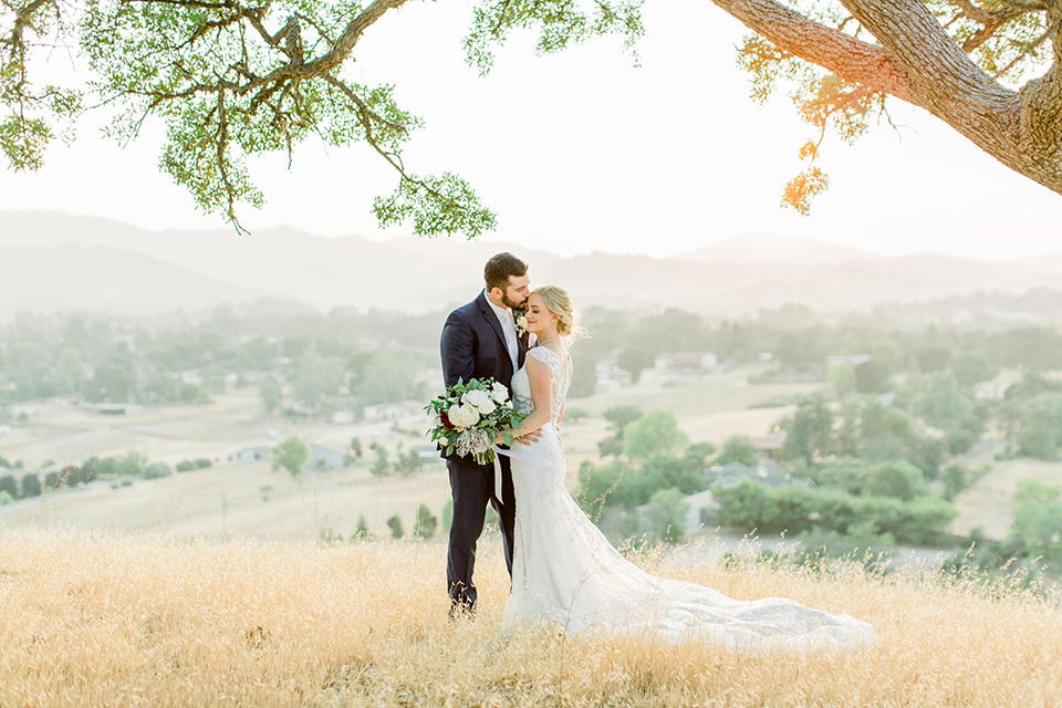 Burgundy-and-Blue-wedding-bride-and-groom-under-tree-bride-in-a-formfitting-white-lace-gown-with-a-strapless-neckline-the-groom-is-in-a-dark-blue-suit-with-an-ivory-long-tie