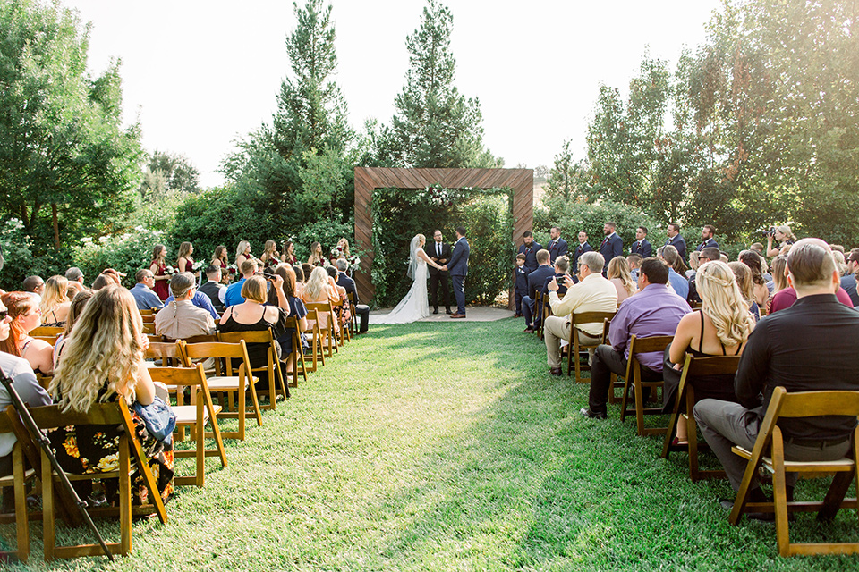 Burgundy-and-Blue-wedding-ceremony-brdesmaids-in-burgundy-gowns-groomsmen-in-dark-blue-suits-bride-in-a-formfitting-white-lace-gown-with-a-strapless-neckline-the-groom-is-in-a-dark-blue-suit-with-an-ivory-long-tie