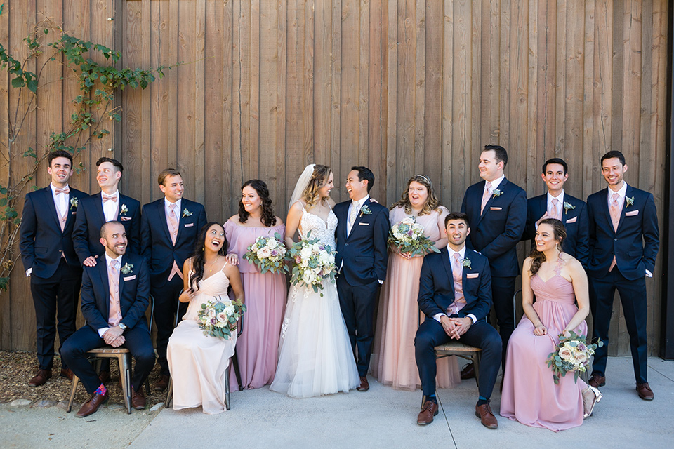 Garden-Wedding-bridalparty-standing-bridesmaids-in-pink-long-dresses-groomsmen-are-in-navy-suits-with-pink-vests-and-pink-bow-ties-bride-in-a-strapless-ballgown-and-groom-in-a-navy-suit-with-a-white-long-tie