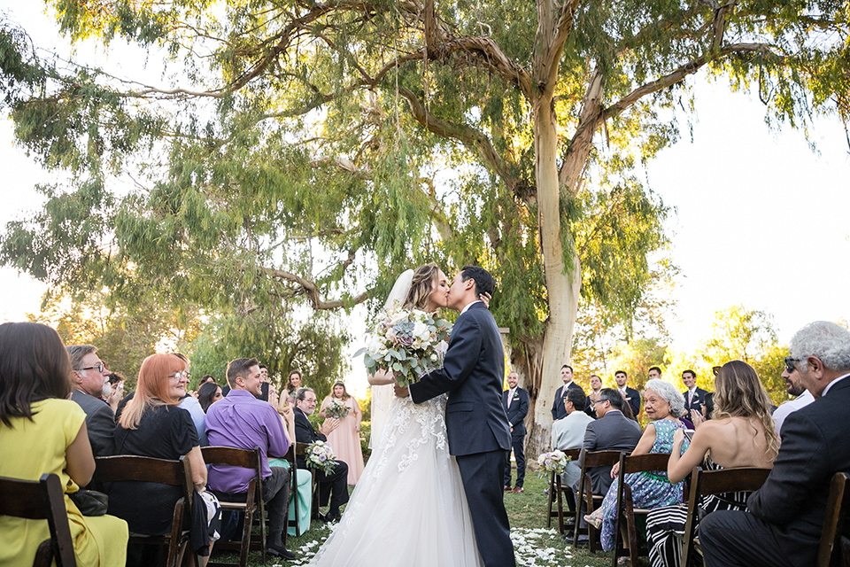 Garden-Wedding-bride-and-groom-ceremony-bridesmaids-in-pink-long-dresses-groomsmen-are-in-navy-suits-with-pink-vests-and-pink-bow-ties-bride-in-a-strapless-ballgown-and-groom-in-a-navy-suit-with-a-white-long-tie