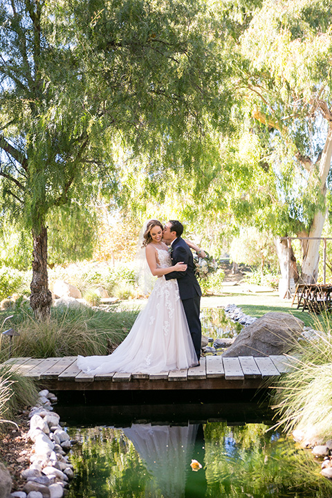 Garden-Wedding-bride-and-groom-standing-on-bridge-bride-in-a-strapless-ballgown-with-her-hair-down-in-a-loose-wave-groom-in-a-navy-suit-with-a-white-long-tie-and-pink-pocket-square