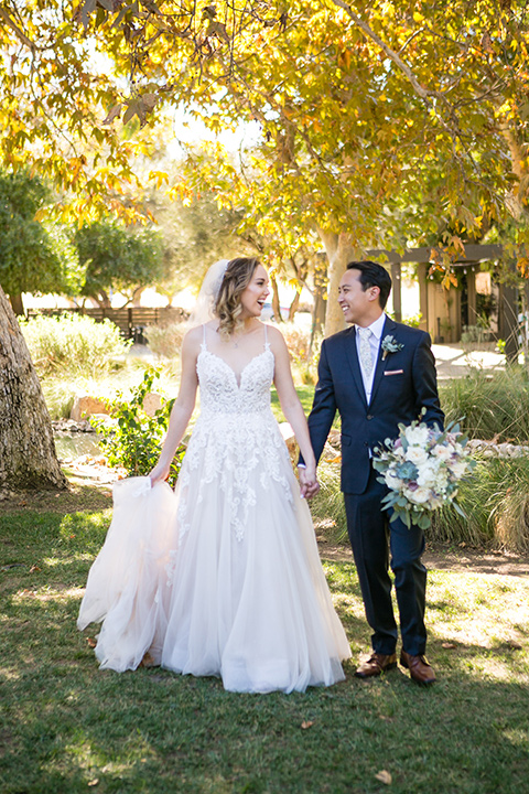 Garden-Wedding-bride-and-groom-walking-bride-in-a-strapless-white-ballgown-and-the-groom-in-a-navy-suit-with-a-white-long-tie-and-pink-pocket-square