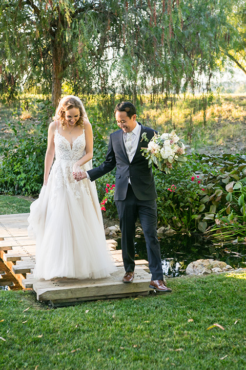 Garden-Wedding-groom-walking-with-bride-bride-in-a-strapless-white-ballgown-and-the-groom-in-a-navy-suit-with-a-white-long-tie-and-pink-pocket-square