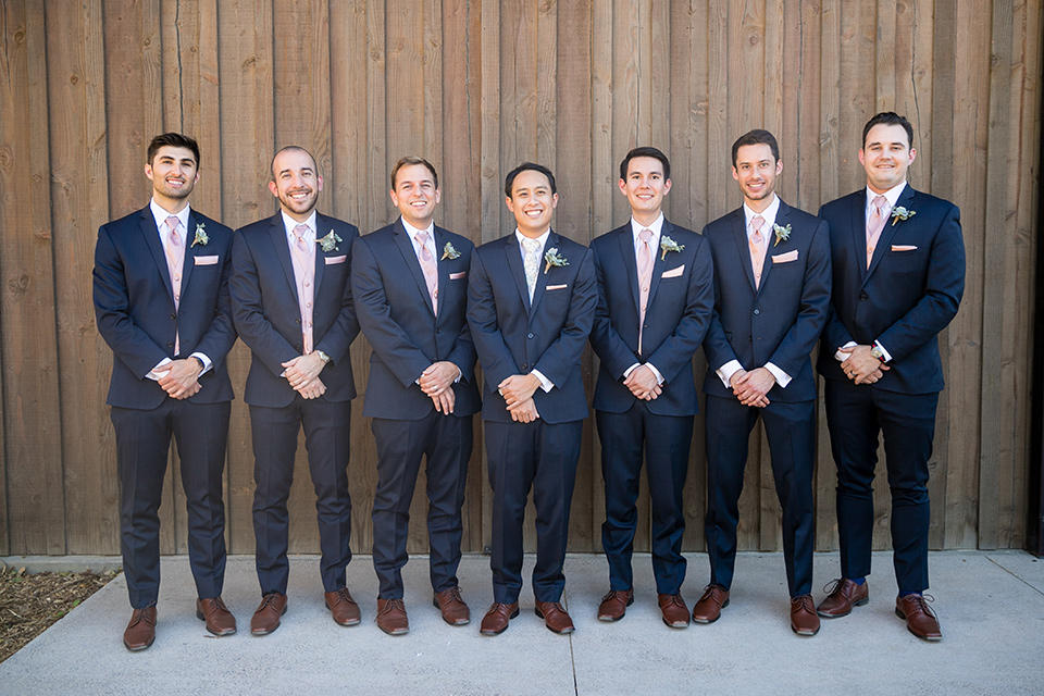 Garden-Wedding-groomsmen-in-a-line-groomsmen-are-in-navy-suits-with-pink-vests-and-pink-bow-ties-and-groom-in-a-navy-suit-with-a-white-long-tie