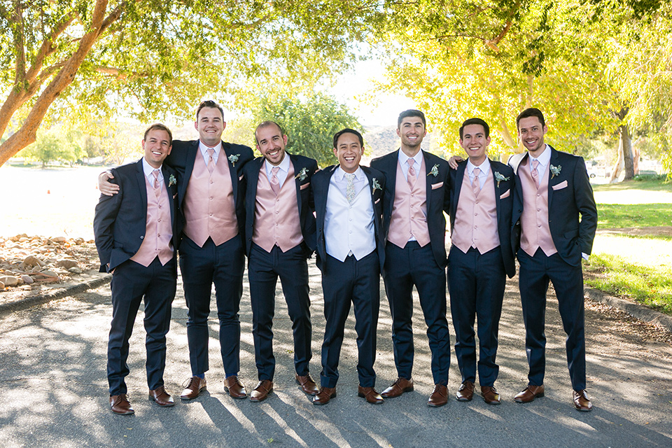 Garden-Wedding-groomsmen-standing-groomsmen-in-a-line-groomsmen-are-in-navy-suits-with-pink-vests-and-pink-bow-ties-and-groom-in-a-navy-suit-with-a-white-long-tie