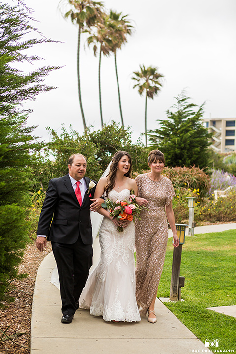 Bride walks down the aisle in a white gown with her parents