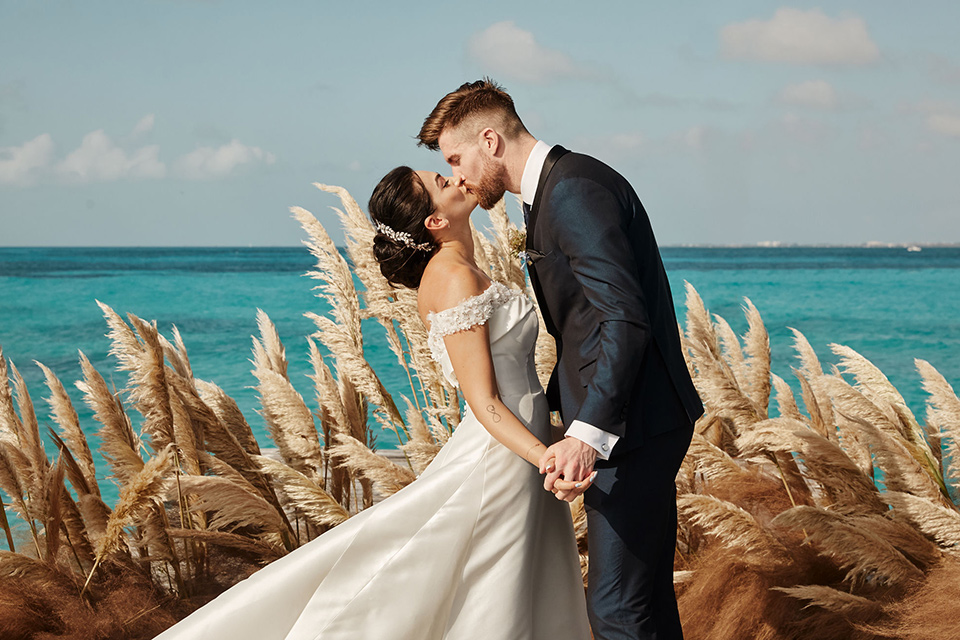 Grand-Firesta-Americana-Coral-Beach-couple-ceremony-kiss-groom-in-navy