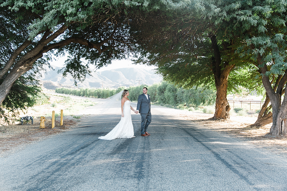 gallaway-downs-wedding-bride-and-groom-walking-across-the-road-bride-in-a-lace-a-line-gown-and-groom-in-a-navy-blue-suit-with-a-white-long-tie