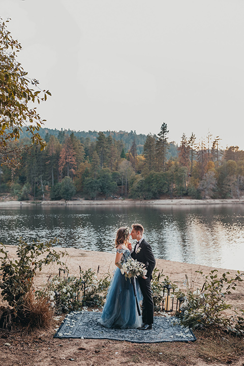 Big-Bear-Elopement-Shoot-bride-and-groom-in-carpet-ceremony-space-bride-wearing-a-blue-tulle-gown-with-an-illusion-neck-line-and-floral-design-groom-with-black-tuxedo-and-black-bow-tie