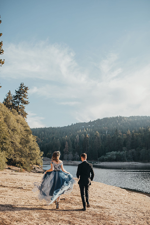 Big-Bear-Elopement-Shoot-bride-and-groom-running-bride-wearing-a-blue-tulle-gown-with-an-illusion-neck-line-and-floral-design-groom-with-black-tuxedo-and-black-bow-tie