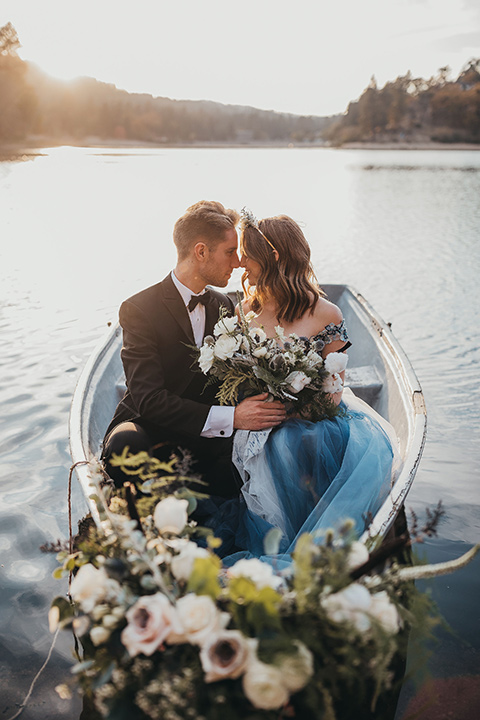 Big-Bear-Elopement-Shoot-bride-and-groom-sitting-in-boat-bride-wearing-a-blue-tulle-gown-with-an-illusion-neck-line-and-floral-design-groom-with-black-tuxedo-and-black-bow-tie