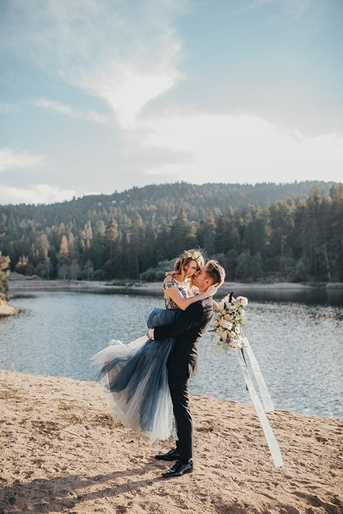 Big-Bear-Elopement-Shoot-groom-lifting-up-bride-the-bride-is-in-a-blue-tulle-gown-with-an-illusion-neckline-and-floral-design-the-groom-wore-a-traditional-black-tuxedo-with-a-peak-lapel-and-black-bow-tie