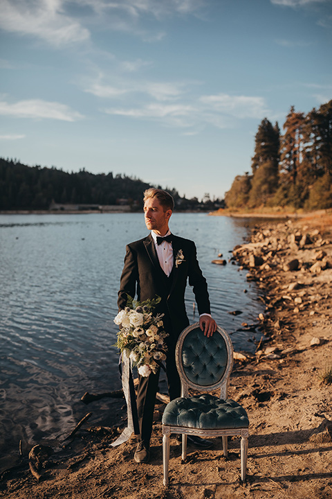 Big-Bear-Elopement-Shoot-groom-standing-by-chair-in-a-traditional-black-tuxedo-with-a-peak-lapel-and-black-bow-tie