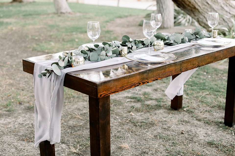 Blomgren Ranch wedding table set up with wood tables in a picnic style with white and green florals and silver flatware