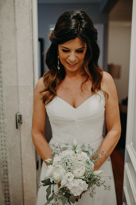 West-Hollywood-Wedding-bride-looking-at-her-flowers-in-a-flowing-white-gown-with-straps