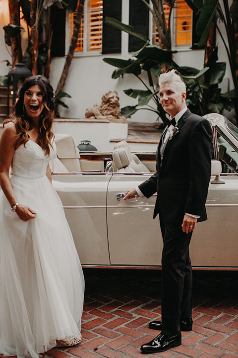 West-Hollywood-Wedding-bride-opening-the-car-door-one-bride-in-a-black-tuxedo-with-a-grey-cvest-and-black-bow-tie-the-other-bride-in-a-flowing-white-gowin-with-a-sweetheasrt-neckline-and-white-straps