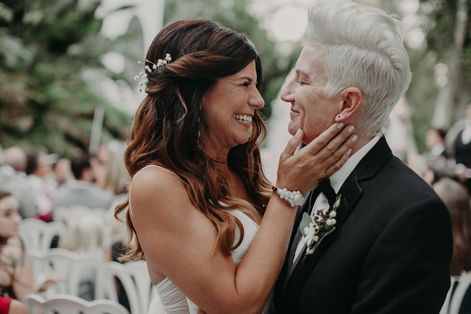 West-Hollywood-Wedding-brides-close-up-one-bride-in-a-black-tuxedo-with-a-grey-vest-and-black-bow-tie-the-other-bride-in-a-flowing-white-gown-with-a-sweetheart-neckline-and-white-straps