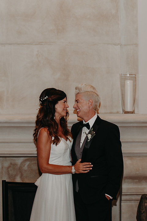 West-Hollywood-Wedding-brides-looking-at-each-other-one-bride-in-a-black-tuxedo-with-a-grey-cest-and-black-bow-tie-the-other-bride-in-a-flowing-white-gowin-with-a-sweetheasrt-neckline-and-white-straps