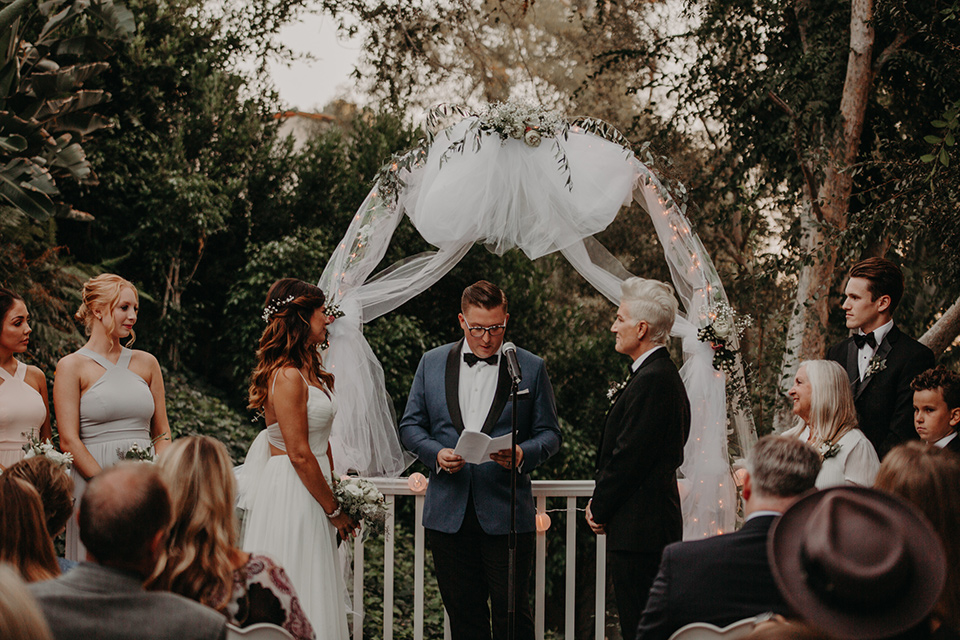 West-Hollywood-Wedding-ceremony-one-bride-in-a-black-tuxedo-with-a-grey-vest-and-black-bow-tie-the-other-bride-in-a-flowing-white-gowin-with-a-sweetheasrt-neckline-and-white-straps