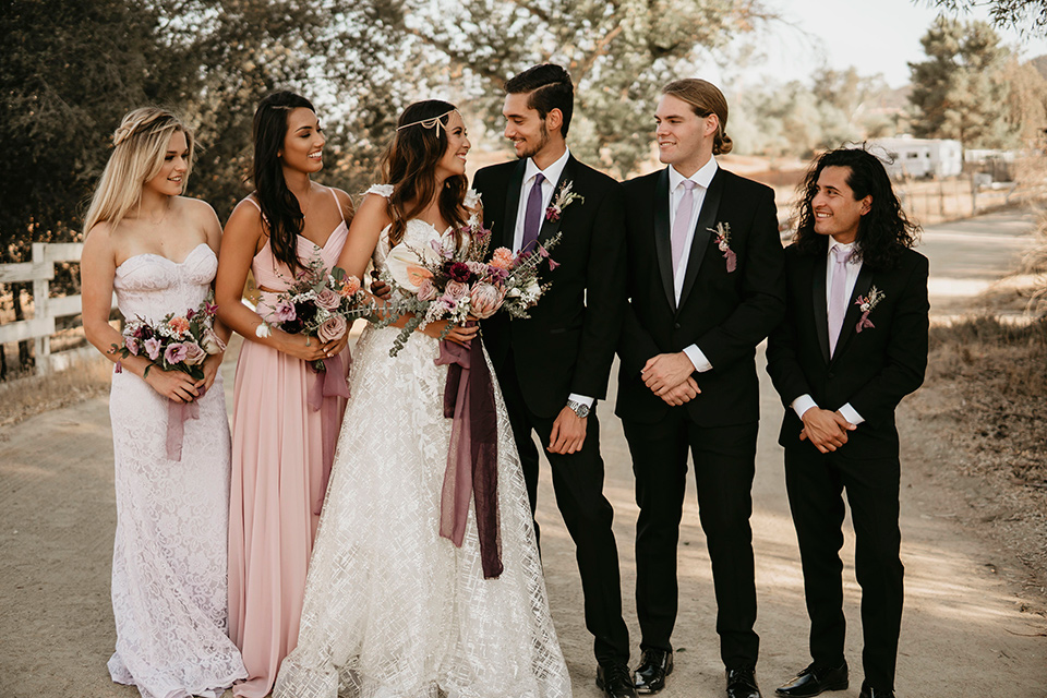 Boho chic elopement wedding with the bridesmaids with soft pink gowns and the groomsmen in black suits the bride in an ivory lace ball gown with a gold chain headpiece and the groom in a black suit with a black long tie