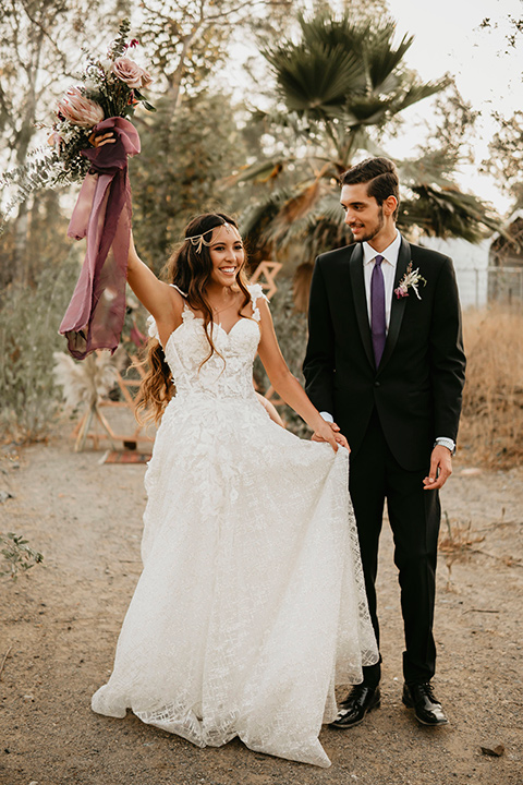 boho elopement shoot with the bride in a lace ball gown and a gold chair headpiece and the groom in a black suit with a long black tie walking away from ceremony