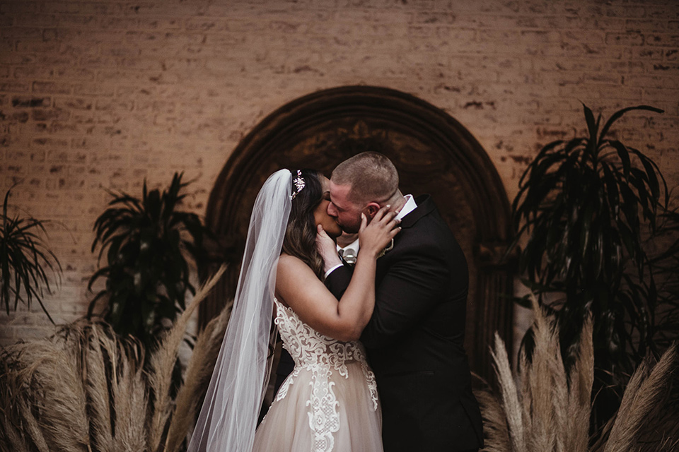 The-Ebell-In-Long-Beach-Wedding-first-kiss-bride-in-a-champagne-ballgown-with-a-strapless-neckline-and-the-groom-in-a-black-tuxedo-with-a-rose-gold-bow-tie