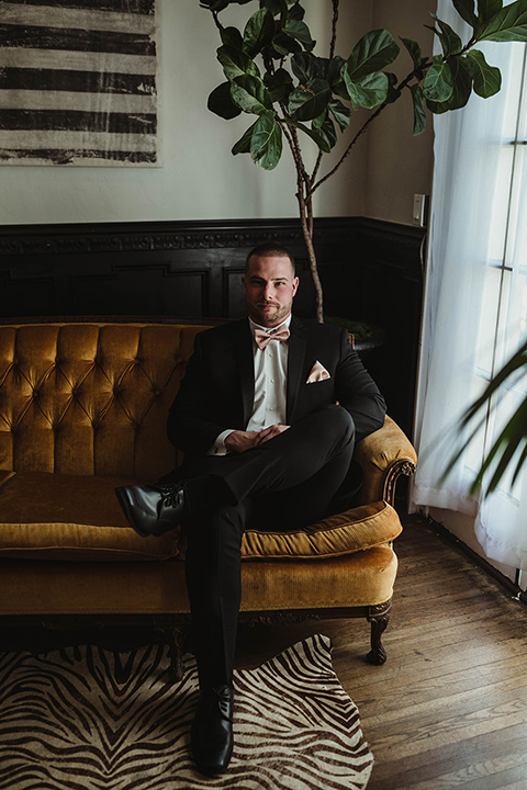 The-Ebell-In-Long-Beach-Wedding-groom-sitting-in-a-black-tuxedo-with-a-rose-gold-bow-tie