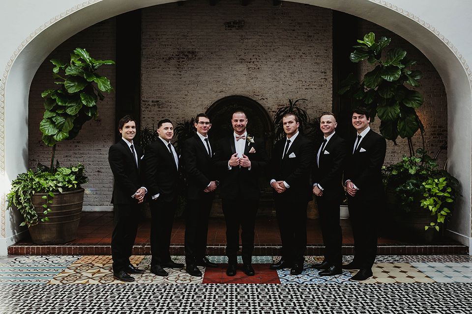 The-Ebell-In-Long-Beach-Wedding-groomsmen-groom-in-a-black-tuxedo-with-a-rose-gold-bow-tie-groomsmen-in-black-tuxedos-with-black-long-ties